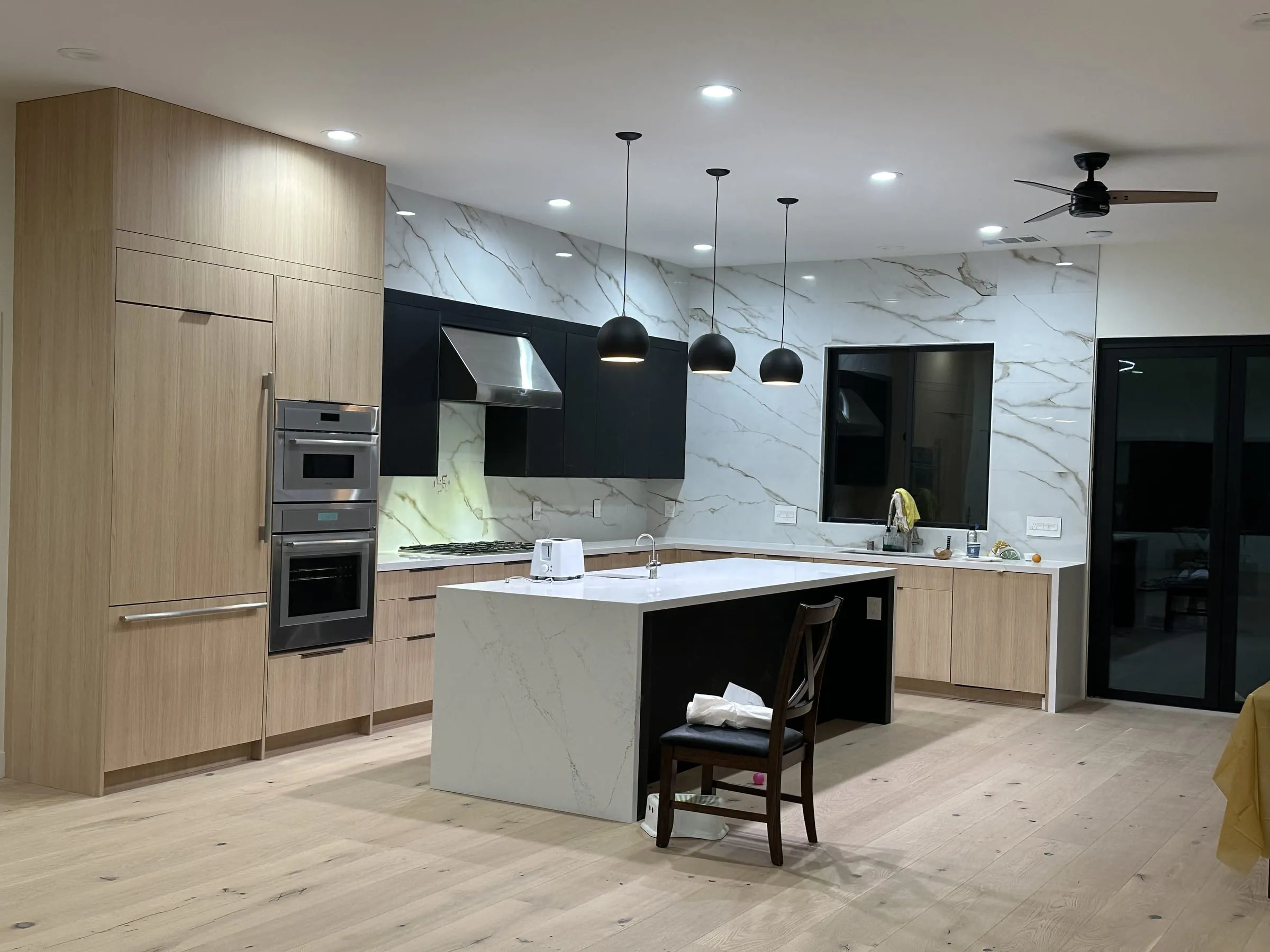 A finished Legacy4Builders kitchen — rift white oak cabinets, black uppers and hood, and a marble-look porcelain slab backsplash run to the ceiling.